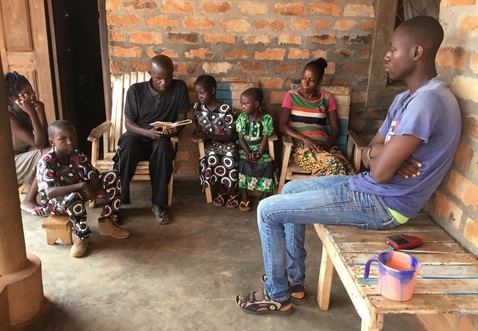 The Rev. Lucien Dockpa (left rear, reading) and intercessor Alapha Aimé de Dieu (right rear) visit with a family at their home in Bangui, Central African Republic, during a daylong evangelism campaign. Photo by the Rev. Cesar Gazza.