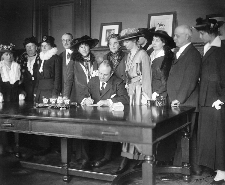 Women bear witness as Gov. Beeckman signs Rhode Island’s Women’s Suffrage Act, April 18, 1917. Behind Gov. Beeckman are (from left) Miss Mabel Ogelman, Senator Henry B. Kane, Mrs. Barton P. Jencks, Elizabeth Upham Yates, Mrs. Edwin C. Smith, Miss Phebe Jencks, Miss Nettie E. Bauer, and Representative Richard W. Jennings. Image from Rhode Island Historical Society Collections, courtesy of Providence College Library.